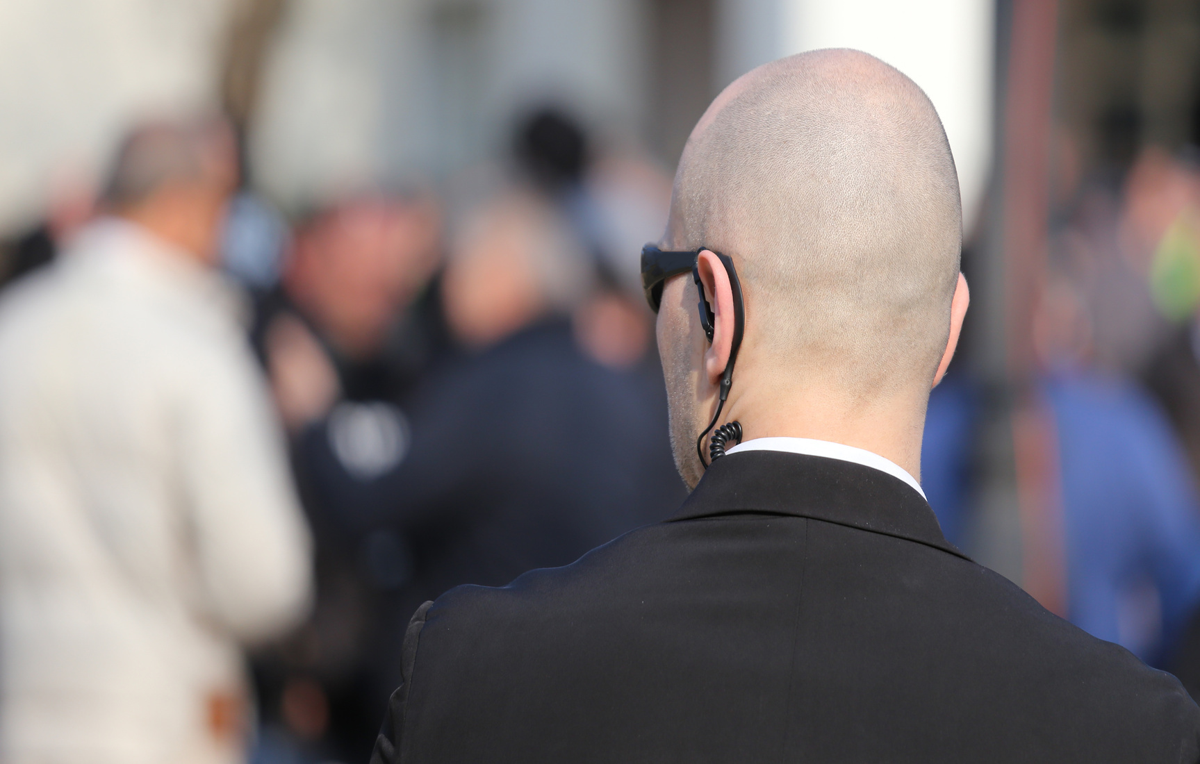 Mann mit Glatze und Ear-Set im Anzug blickt auf Menschenansammlung; Kurtz Detektei Hannover, Detektiv Hannover, Privatdetektiv Hannover, Detektivservice Hannover